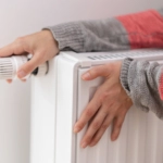 A woman touches a cold radiator of a home heater and increases the heating power